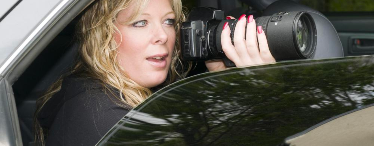 Ruby red fingernails curl around a camera which points out of a car window. The photographer looks surprised with an open mouth and wide green eyes